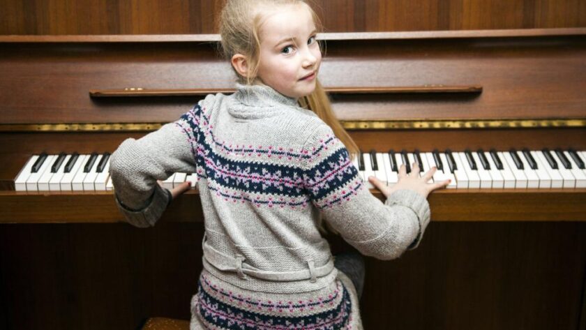 young-girl-sits-at-brown-upright-piano