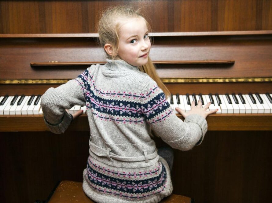 young-girl-sits-at-brown-upright-piano